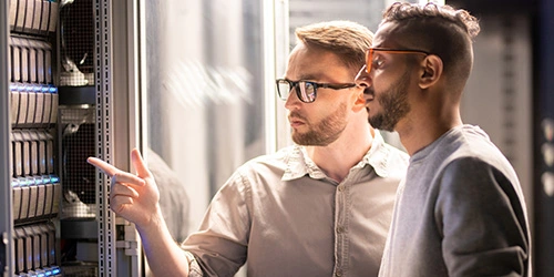 IT professionals reviewing server rack infrastructure and cloud-managed network equipment in a data center
