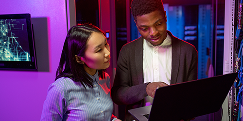 Security team analyzing cyber threat data on a laptop in a modern SOC environment with purple lighting