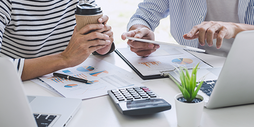 Business team discussing financial reports and cost analysis with calculator and documents on office desk