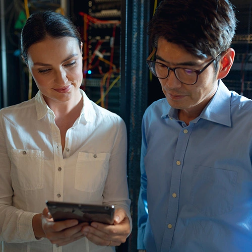 IT professionals reviewing network infrastructure on a tablet inside a modern data center with server racks