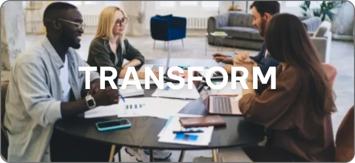 Diverse team collaborating at a round table with laptops and documents, discussing IT transformation strategies. The word 'TRANSFORM' is overlaid on the image.