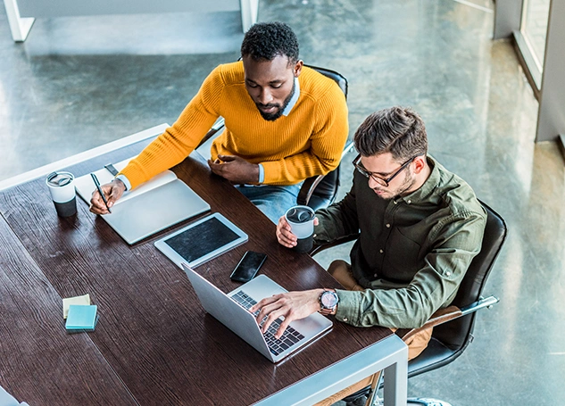 Two professionals reviewing cybersecurity policies on a laptop representing User Application Hardening in the Essential Eight framework.